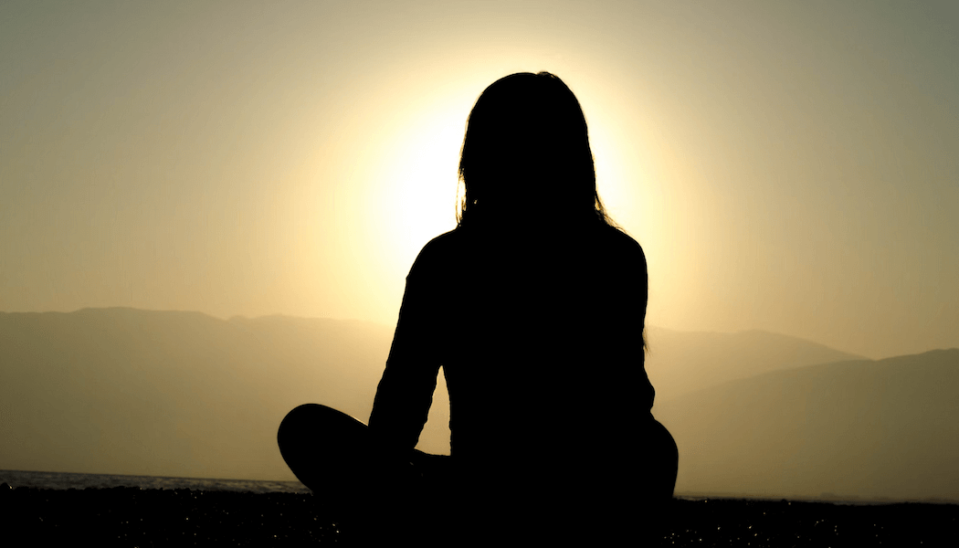 Silhouette of a person meditating at sunrise, symbolizing serenity and stress relief through mindfulness and goal setting.