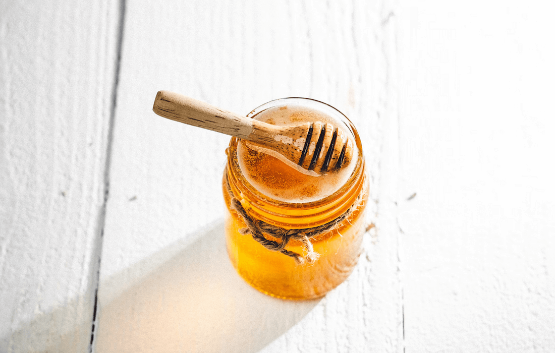 A honey dripper on top of a jar filled with honey.